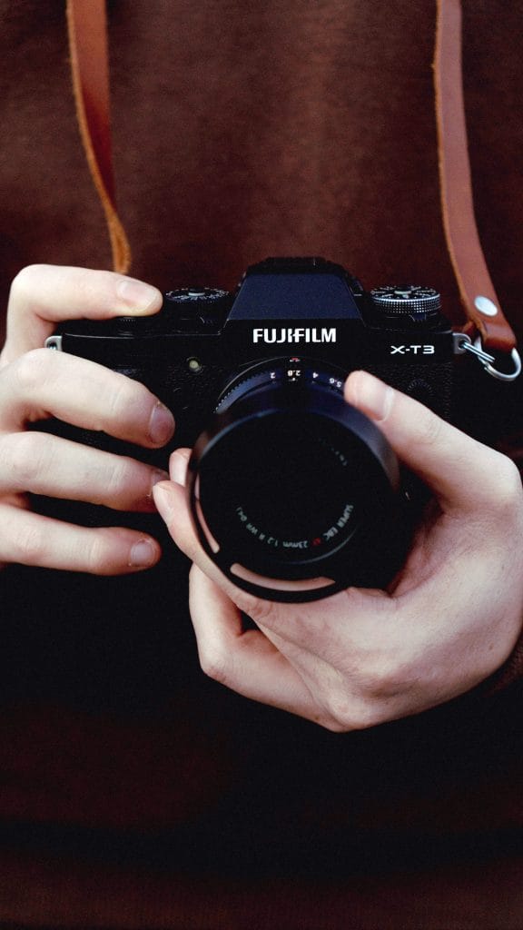 Fujifilm X-T3 - Expert Advice Person holding Fujifilm X-T3 camera in hands while wearing a brown leather camera strap around neck