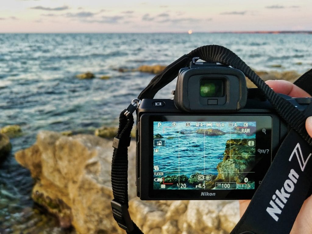 Nikon Z50 - Expert Advice Nikon Z50 camera shown from behind being used to shoot a photo of the ocean