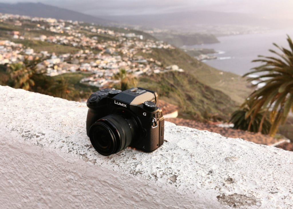 Panasonic Lumix DMC-G85 - Expert Advice Panasonic Lumix DMC-G685 sitting on a ledge overlooking beautiful scenery, including a large body of water.